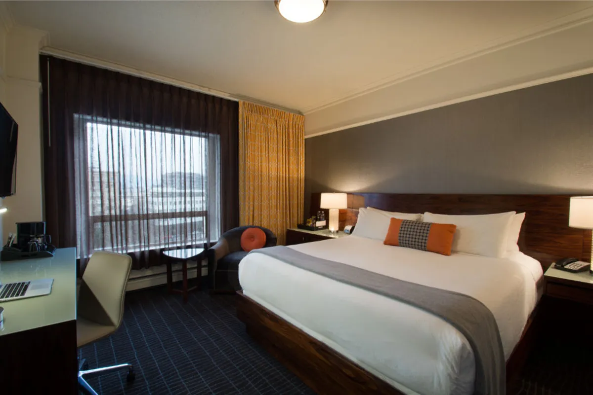 A modern and comfortable guest room with a queen bed, large window, and a functional desk space. The room is bright with daylight, and the setup invites both relaxation and productivity. The desk and window view reinforce the idea of a peaceful retreat that also accommodates work or personal reflection.