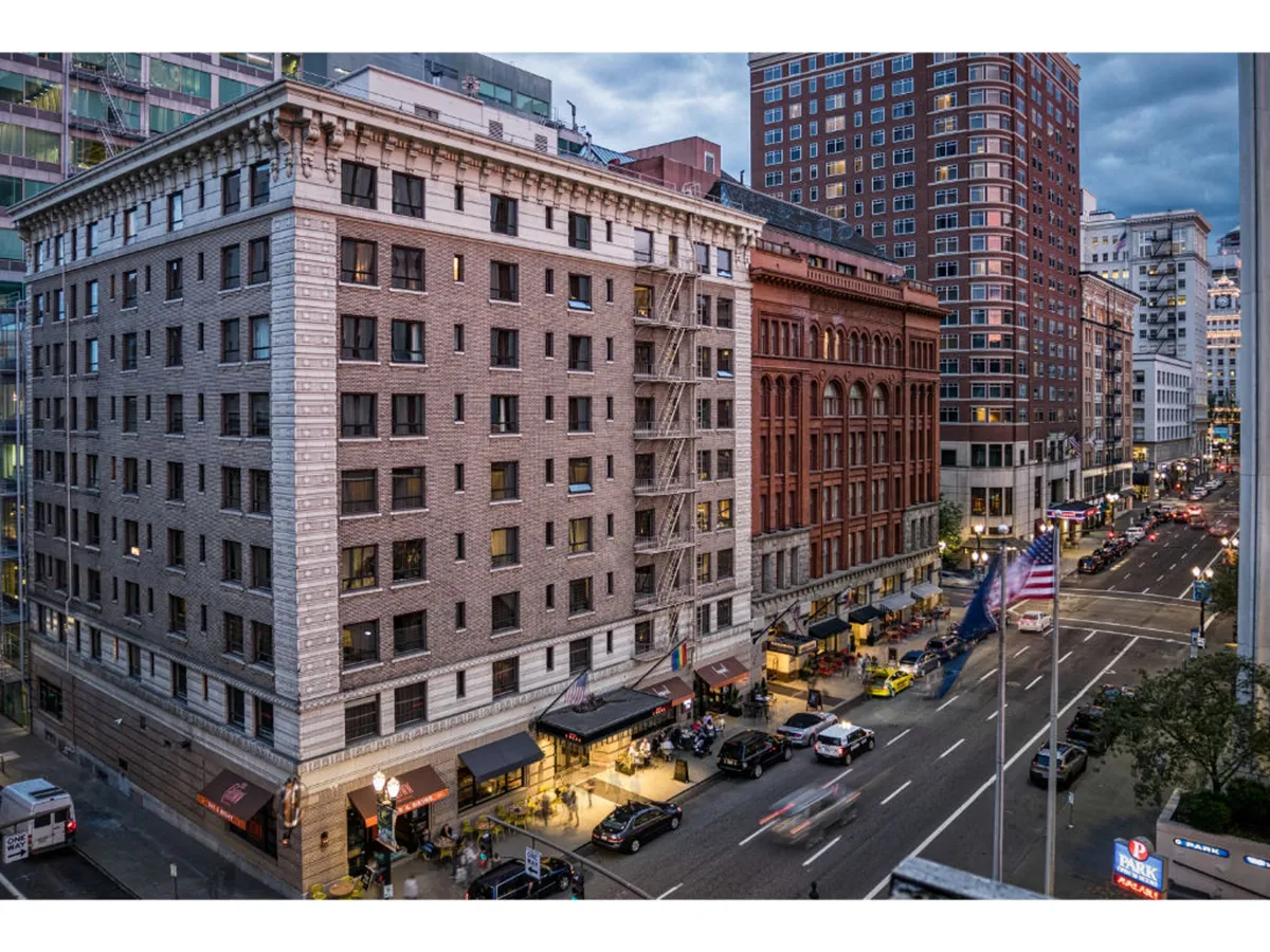 The photo highlights historic building architecture and a lively street bustling with activity. Illuminated storefronts, American flags, and people dining at outdoor cafés evoke the vibrant nightlife and unique shopping experiences that await just steps from the hotel.