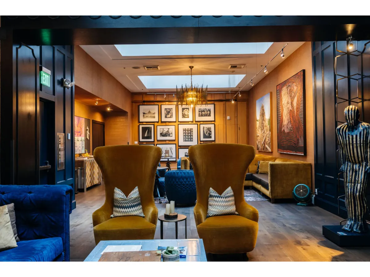 A stylish, art-filled lounge featuring large yellow armchairs, striking artwork on the walls, and a statement chandelier. The open, comfortable setting is ideal for guests and their companions to regroup after a day of discovering Portland.
