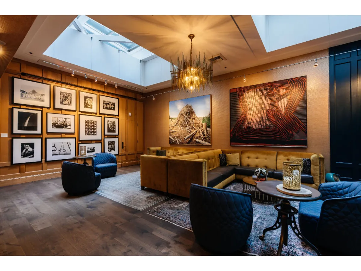 A creative and cozy lounge area with large art pieces on the walls, a plush golden velvet sectional, and a unique chandelier—an inviting space for socializing and appreciating art.