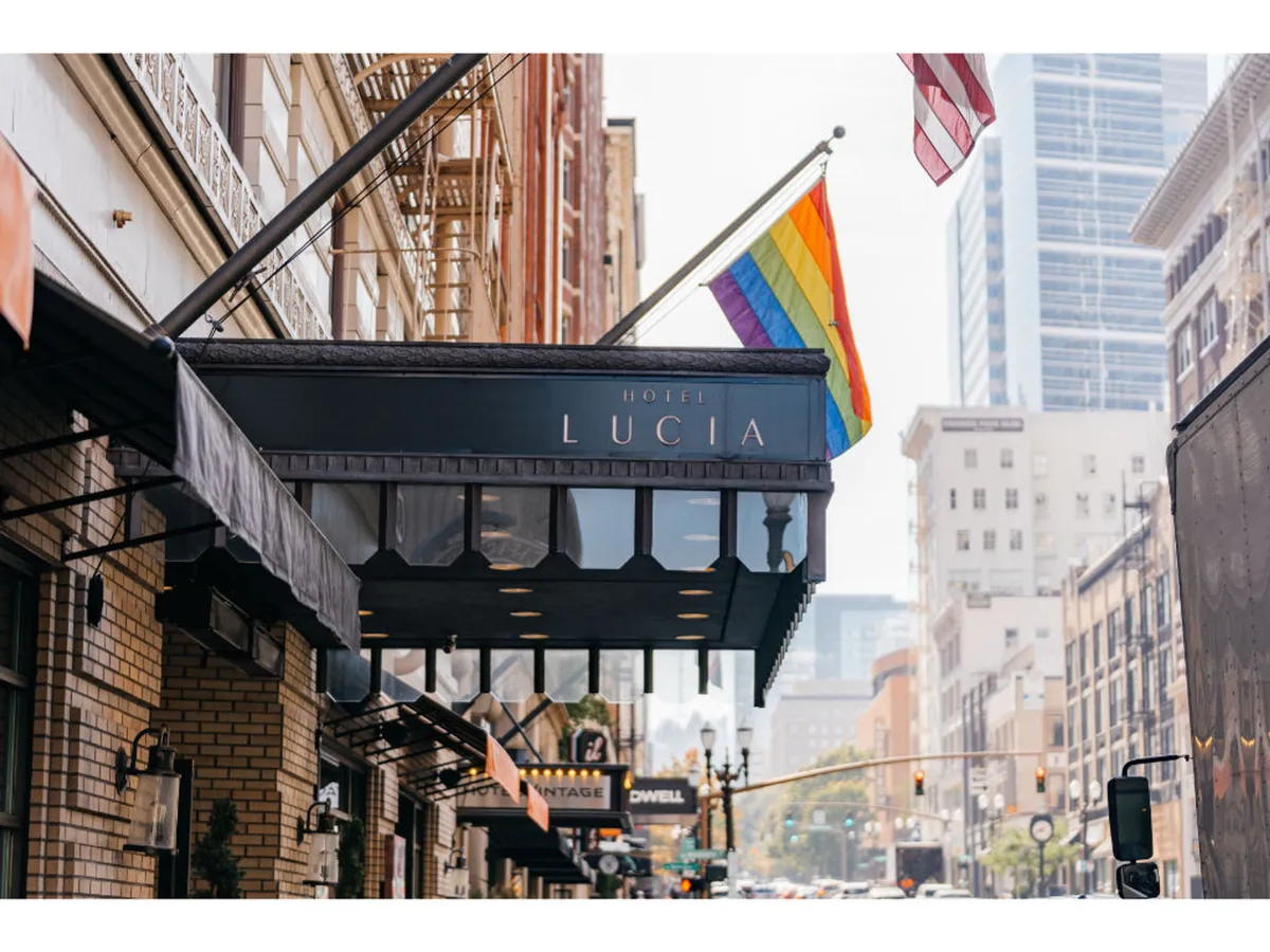 This image captures the exterior of Hotel Lucia, featuring the hotel sign, Pride and American flags, and a lively street scene indicative of downtown Portland's welcoming atmosphere. Pedestrians and hints of nearby shops and restaurants add to the sense of exploration and proximity to local culture.