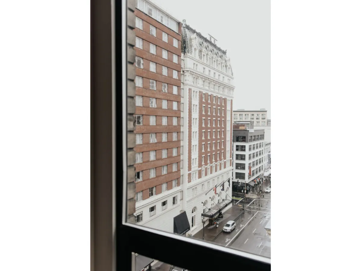A street-level view of historic Portland buildings set against a rain-soaked pavement. The image captures the city's urban charm, inviting exploration of its vibrant surroundings just steps from the hotel.