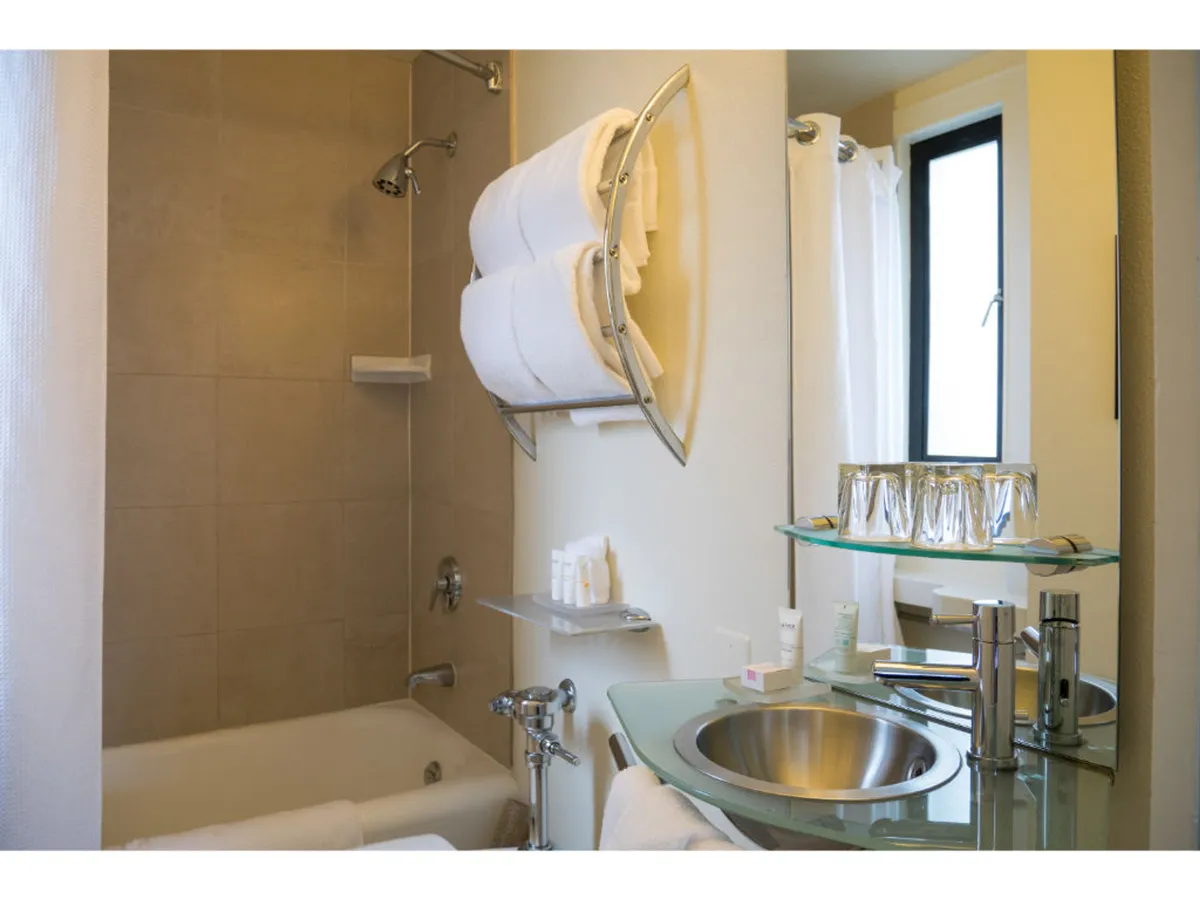 A serene bathroom featuring a bathtub and shower combo, a sink with an elegant mirror, neatly folded towels, and an ambiance that promotes relaxation and self-care. The lighting enhances the refreshing and tranquil atmosphere, ideal for unwinding.